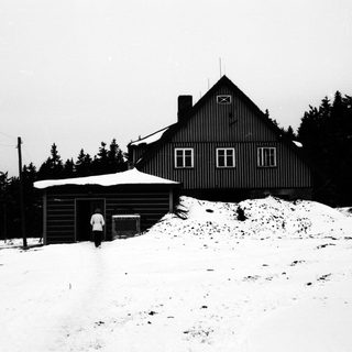 Snow-covered house stands in a winter landscape with trees.