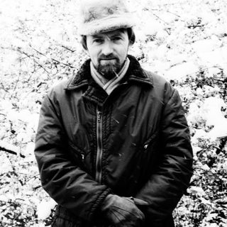 Man in a hat stands in a snowy, wintry landscape.