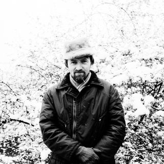 Man in a hat stands in a snowy, wintry landscape.