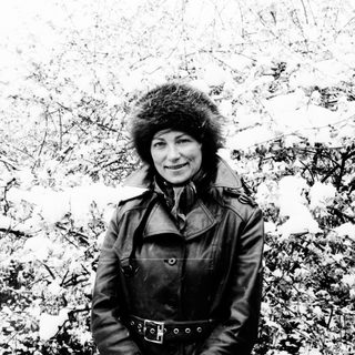 Woman in fur hat stands in a snowy, wintry landscape.