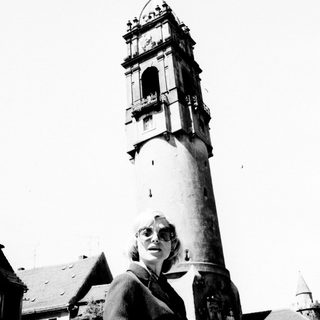 Woman stands before a tall, historic clock tower.