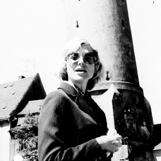 Woman stands before a tall, historic clock tower.