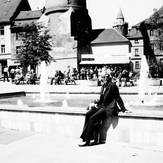 Man sits on fountain wall in a public square.