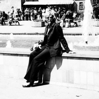 Man sits on fountain wall in a public square.