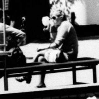 Man sits on fountain wall in a public square.