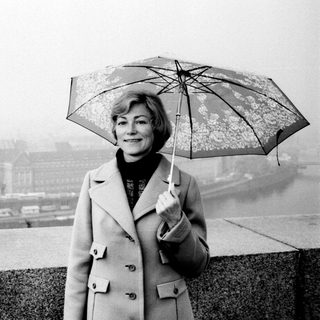 Woman with umbrella stands overlooking a foggy cityscape.