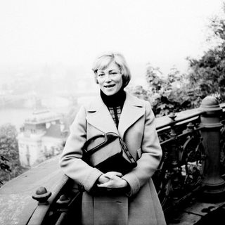 Woman stands on a ledge overlooking a foggy cityscape.