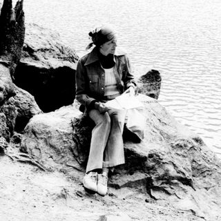 Woman sits on rocks overlooking a body of water.