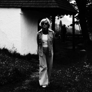 Woman stands near a small, rustic building in a landscape.