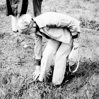 Man bends down in grass, people stand nearby.