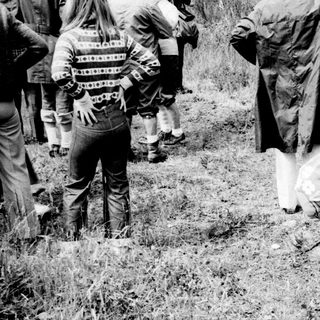 Man bends down in grass, people stand nearby.