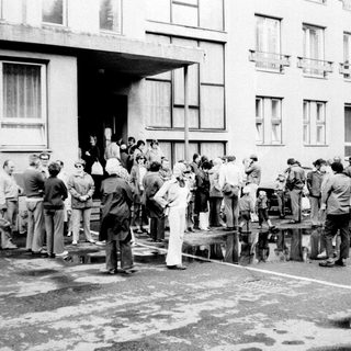 Group of people gathered outside a building, possibly observing something.