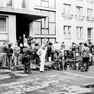 Group of people gathered outside a building, possibly observing something.