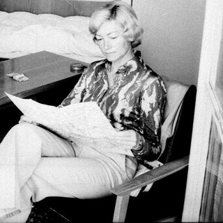 Woman seated reading in a sparsely furnished bedroom.