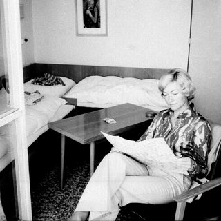 Woman seated reading in a sparsely furnished bedroom.