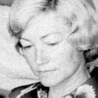 Woman seated reading in a sparsely furnished bedroom.