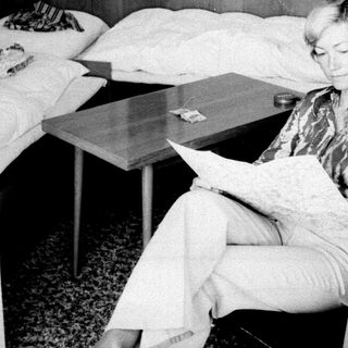 Woman seated reading in a sparsely furnished bedroom.