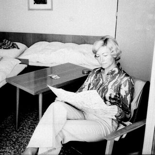 Woman seated reading in a sparsely furnished bedroom.