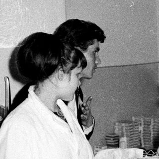 Two women in white coats talk in a kitchen setting.