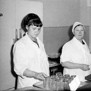 Two women in lab coats working in a vintage kitchen.