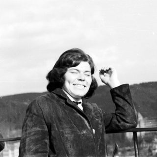 Man smiling, standing by a railing with a landscape behind.