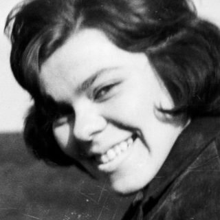 Here's a brief summary of the image: Young woman smiles outdoors with a landscape in background.