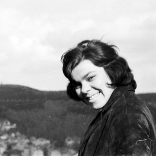 Here's a brief summary of the image: Young woman smiles outdoors with a landscape in background.