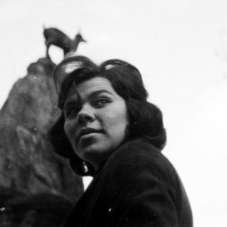 Woman poses near a statue with a dog on top.