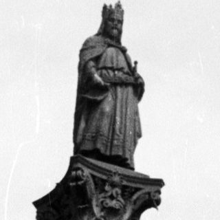 Here's a brief summary of the image: Woman sits atop a monument with a statue.