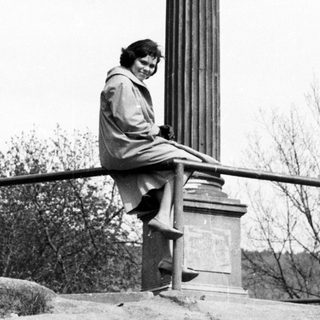 Here's a brief summary of the image: Woman sits atop a monument with a statue.
