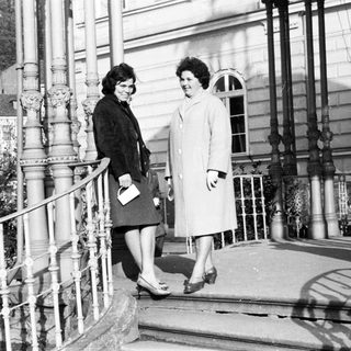 Two women in coats stand on a stone staircase.