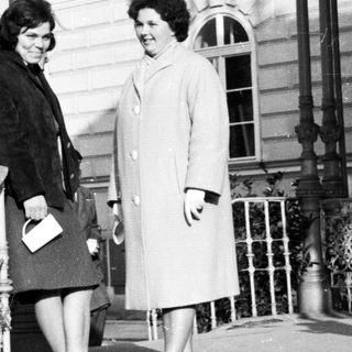 Two women in coats stand on a stone staircase.