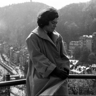 Woman in coat overlooks city from a balcony.