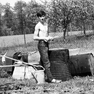 Man stands near debris in a wooded, rural area.