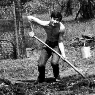 Man working in a garden with tools and debris.