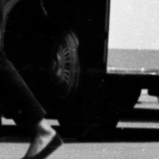 Black and white image of buses and people standing nearby.