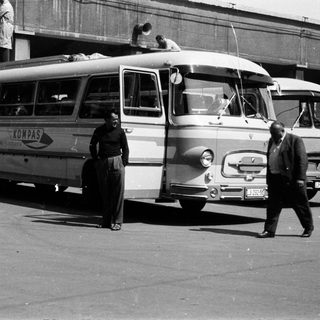 Black and white photo of buses and people in a street.