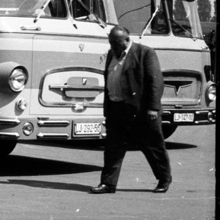 Black and white photo of buses and people in a street.