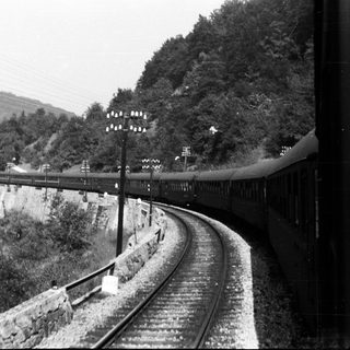 Black and white image of a train curving along a river.