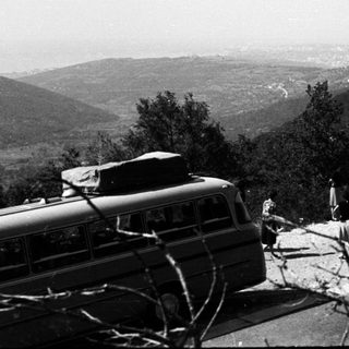Group gathers near bus and car on a scenic road.