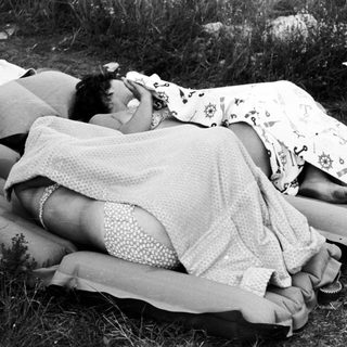 Woman sunbathing on inflatable mattresses in a grassy area.