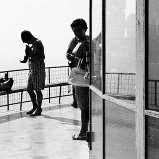 Two women stand on a balcony with a view.