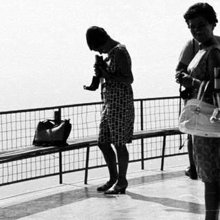 Two women stand on a balcony with a view.