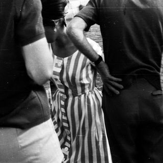 Here's a brief summary of the image: Man in striped dress being escorted, seemingly restrained.