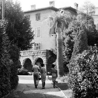 Two figures walk along a path towards a large estate.