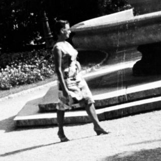 Woman sits near a statue in a park.