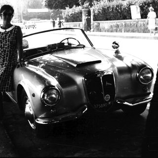 Woman stands beside vintage car on a public street.