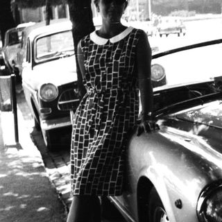 Woman stands beside vintage car on a public street.