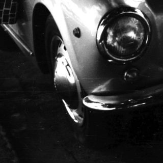 Woman stands beside vintage car on a public street.