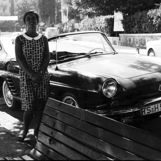 Woman stands beside vintage car in black and white photograph.